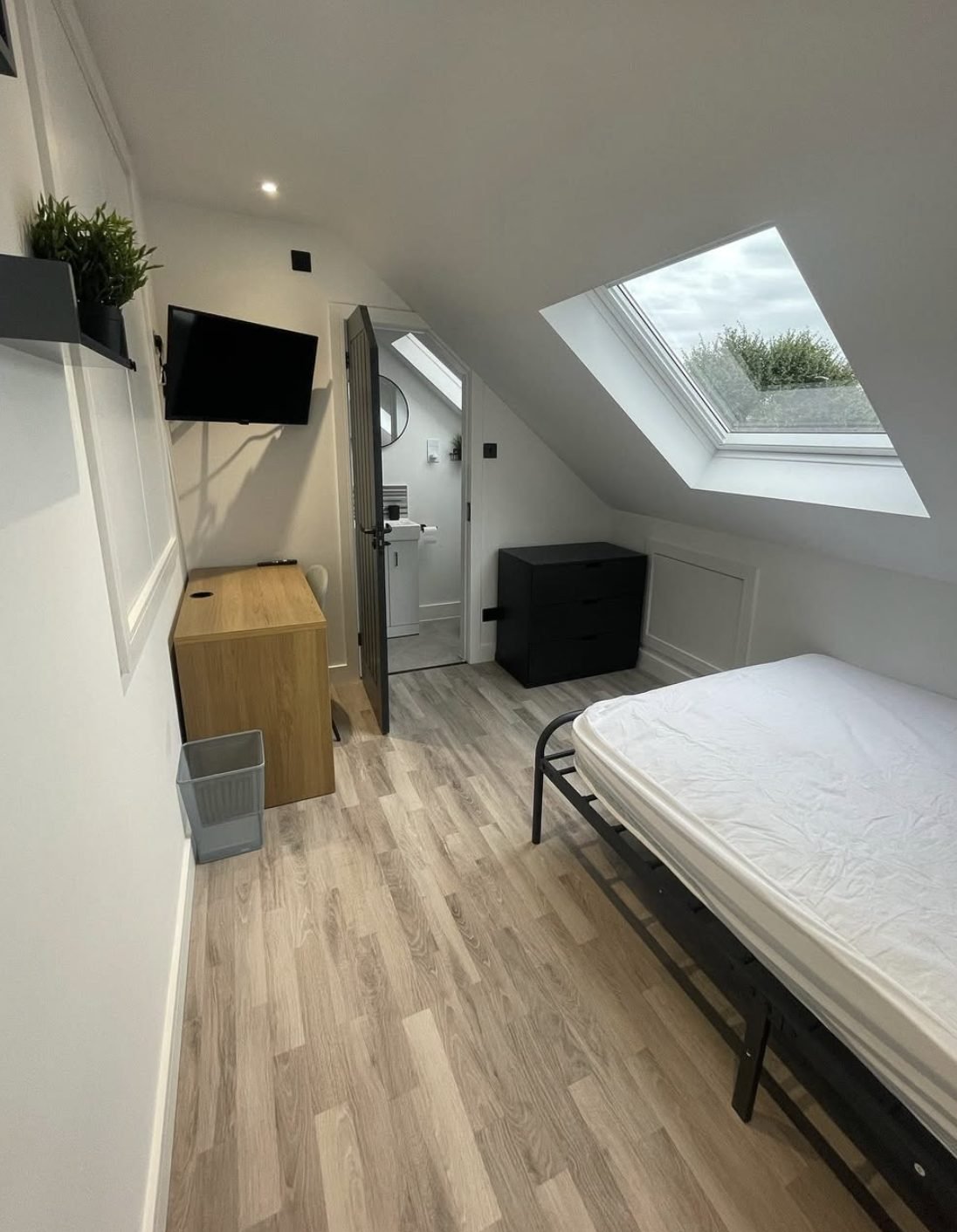 Finished loft bedroom with rooflight, wood-effect flooring, panelled walls and a door through to a loft shower room