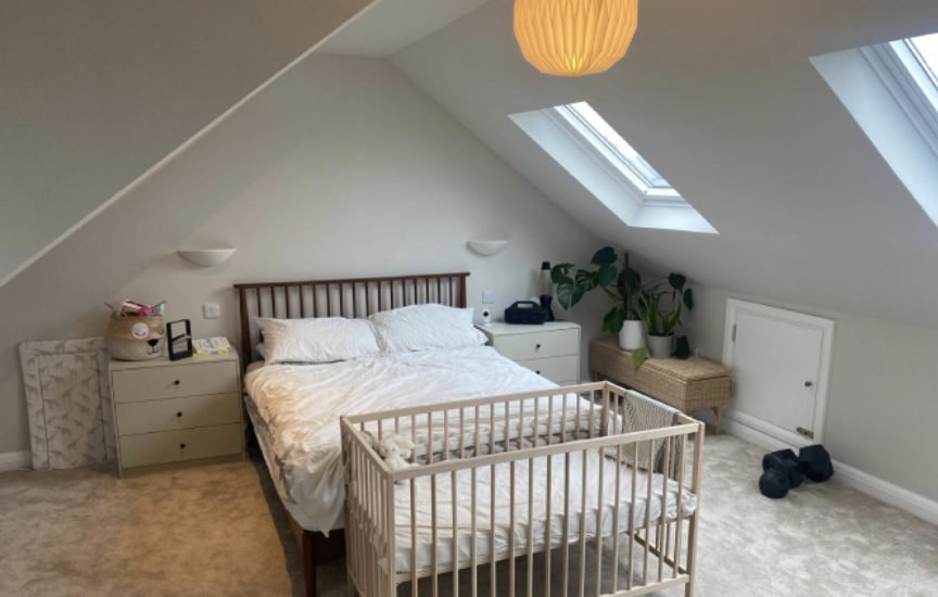 Bright loft bedroom with two rooflights, sloping ceilings, double bed and a cot in the corner