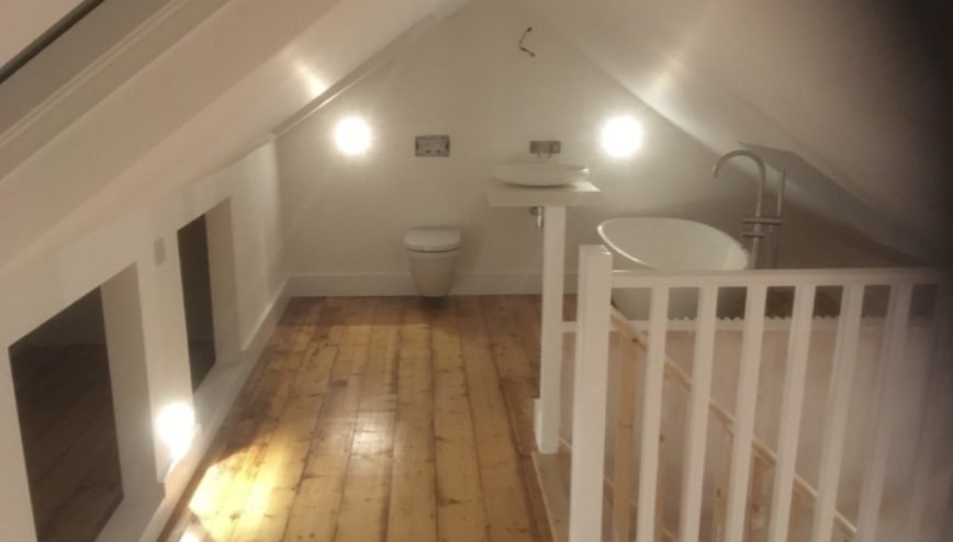 Loft bathroom under the eaves with wall-hung WC, basin and freestanding bath beside the new staircase