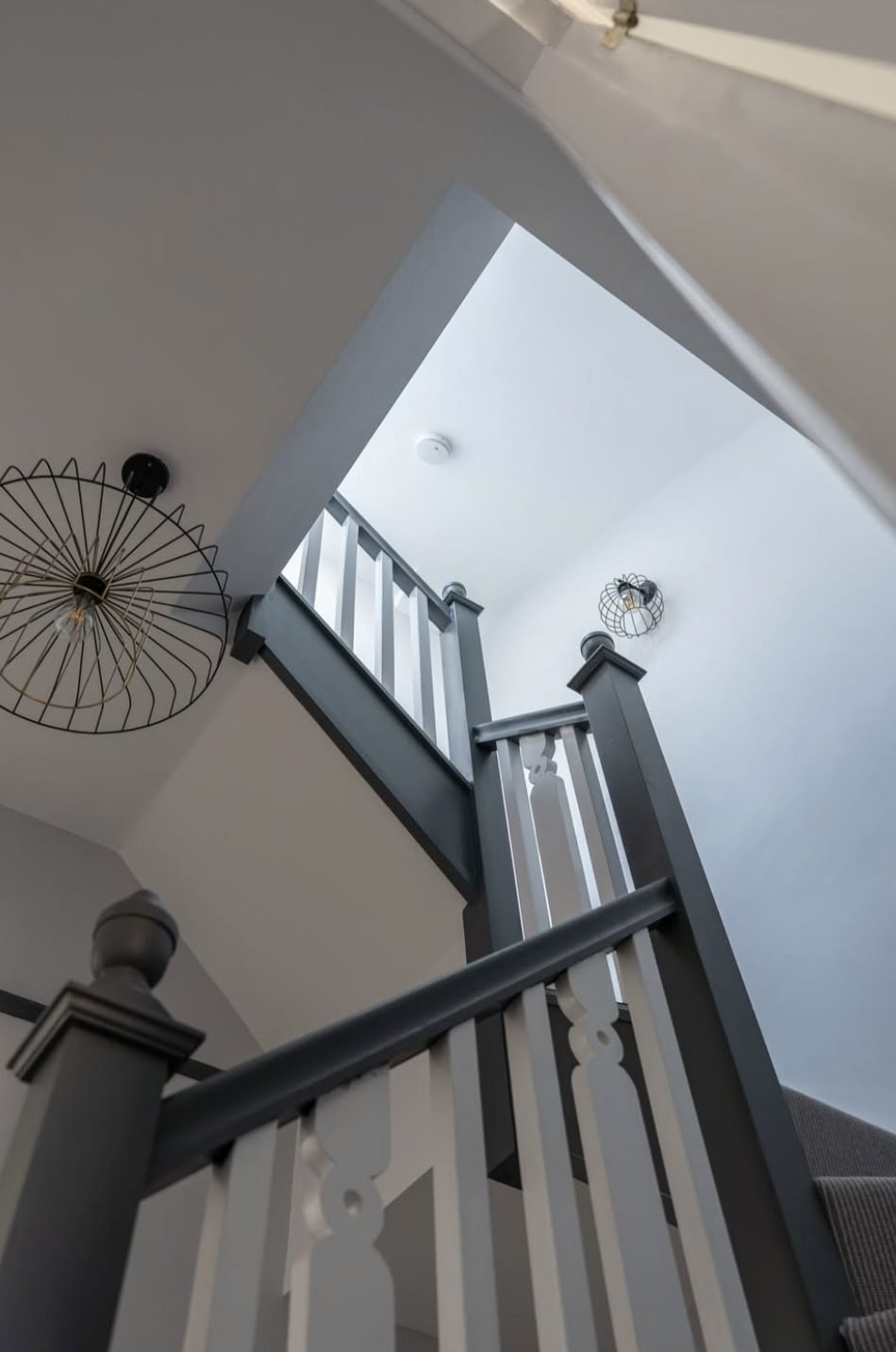 Looking up a loft staircase with grey painted handrail and newels, white spindles and a wire pendant light